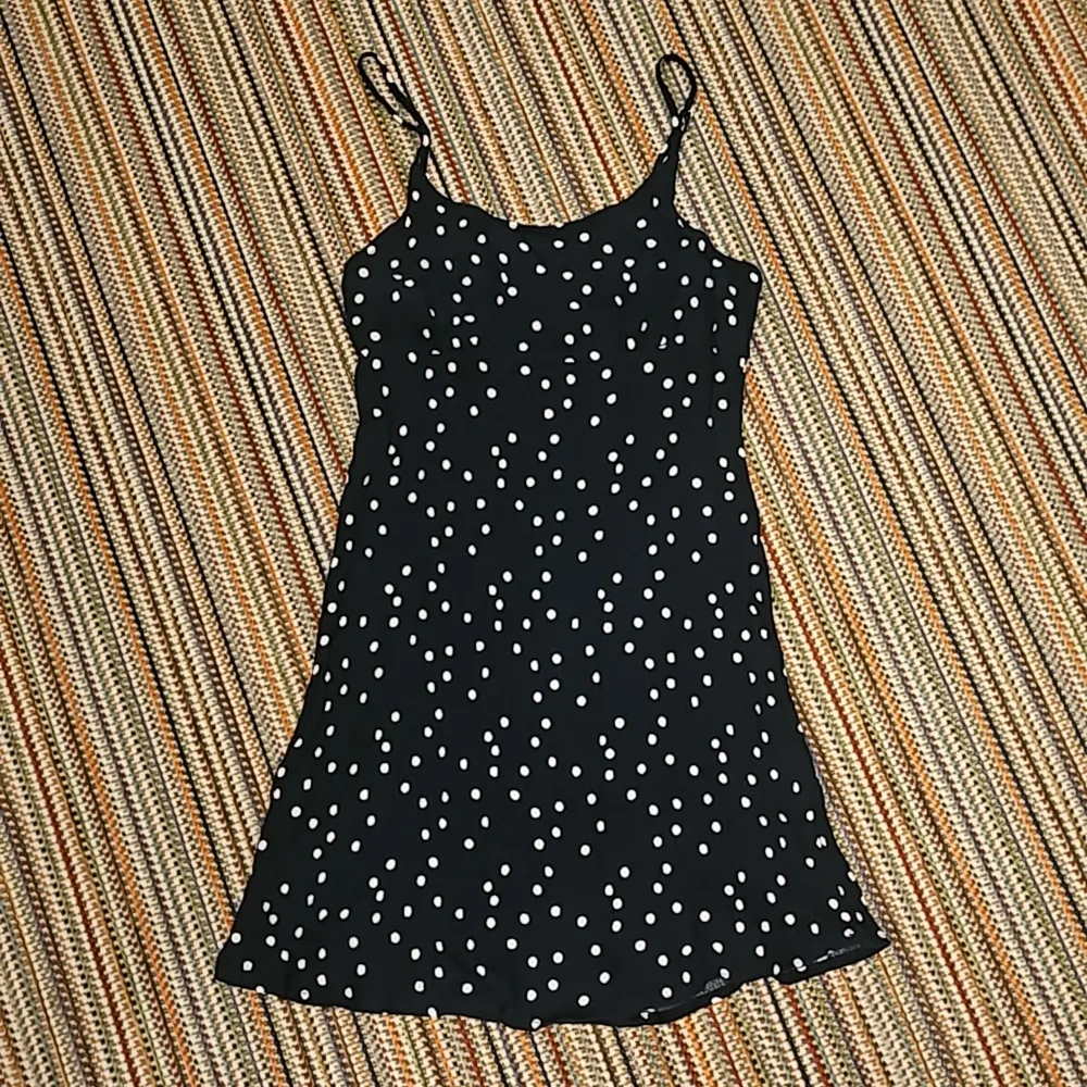 En mörkblå kläning som nästan ser svart ut och som har vita prickar på sig. Den har lite stretch i sig och en dragkedja där bak.. Klänningar.