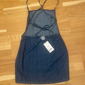Miniklänning i denim med band - Helt oanvänd med prislapp kvar, normal i storleken. Osynlig dragkedja i midjan, samt resår där bak i midjan. Superfin nu till sommaren/våren knyts förslagsvis som på bild ett 🌸