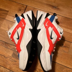 Nike M2K Tekno Sneakers - Nike M2K Tekno Sneakers i vit färg med blå, orange och svarta detaljer.  Sneakersen är köpta second hand men EJ ANVÄNDA av mig. Lite noppriga vid hälen men inget som påverkar användningen. (Se bild nummer 2.) samt inga sulor.