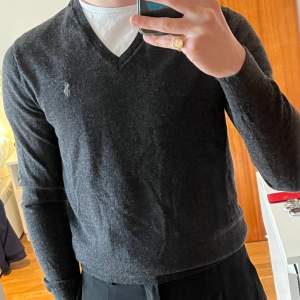 Mörgrå v-neck jumper i merino ull från ralph lauren. I princip oanvänd p.ga storlek. Tröjan är storlek S och sitter tajt på mig (181 cm). Inga fel.