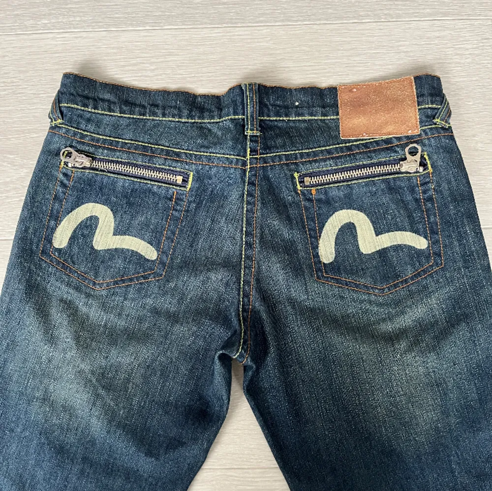 Dösnygga äkta Evisu jeans med coola detaljer! Jeansen är lågmidjade och har greenwash. De är i mycket bra skick med inga skador.  Raktöver midjan: 43cm the flare raktöver: 22cm ytterbenslängd: 95cm Kontakta vid frågor och intresse<3. Jeans & Byxor.