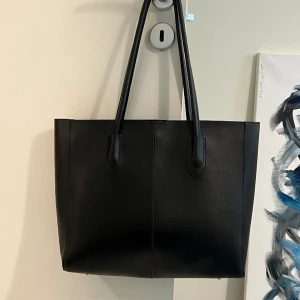 Stilren, rymlig och elegant läderväska! - En rymlig, tidlös och elegant svart lädertotebag (PU-läder) i oanvänt skick! Fick den i julklapp 2023 och är oanvänd då jag redan har en liknande väska! Bara höra av dig om du har frågor eller vill ha fler bilder! 32 x 29 cm ! 🖤