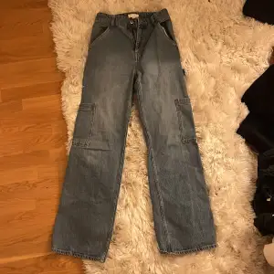 Ett par mellanblå baggy jeans i storlek 34 (EUR). De har sammanlagt 7 fickor. 