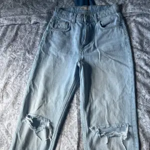 Högmidjade slitna straight jeans med hål från Gina Tricot i storlek 34, nyskick utan defekter.