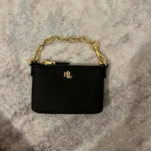Ralph Lauren väska/plånbok - Säljer denna Ralph lauren väska/plånbok. Den e i mycket bra skick, lädret e som helt nytt och det guldiga runt om är som helt nytt också! Den funkar att ha som plånbok då den är liten och smidig att ha i t,ex fickan. Nypris 1200 mitt pris endast 250