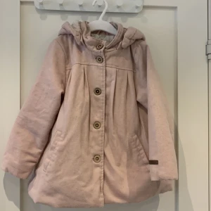 Kappa newbie  - Jättefin ljusrosa kappa från newbie med foder och lurvig luva. Den är använd endast några gånger. Det är 50% ull därav något luddig, ull blir det lätt även efter första tvätten. 