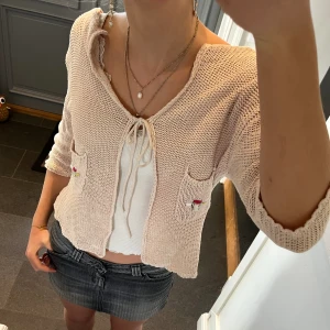 Beige stickad kofta  - Beige/rosa stickad kofta med snörning från Millenium. Kan inte hitta storlek men skulle säga S, passar även M. Fint skick. Använd gärna köp nu!