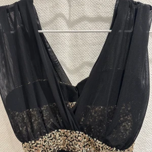 Svart festklänning med guld - Svart guldglittrande klänning.  Elastiskt tyg, rynkad i sidan. Guld med paljetter. 