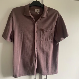 Brun kortärmad skjorta från H&M - En brun/lila kortärmad skjorta från H&M i storlek S. Skjortan har en bröstficka och knappar framtill. Den är av regular fit-modell. bra skick