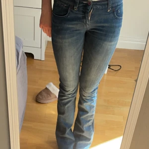 Blå jeansbyxor - Ett par blå jeansbyxor med en tight passform och utsvängda ben. Byxorna har en klassisk femficksdesign och stängs med dragkedja och knapp. de är även lågmidjade