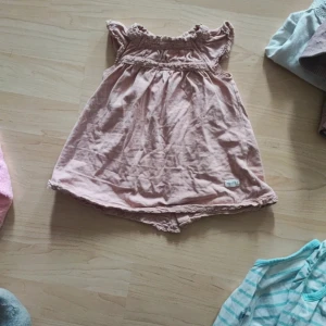 Rosa klänning från Newbie - En söt rosa klänning från Newbie i storlek 62. Klänningen har korta ärmar och knappar på baksidan. Den har även fina spetsdetaljer vid ärmslut och nederkant. utan anmärkningar 