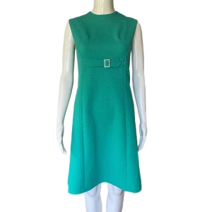 Klänning  - En äldre klänning i fint skick. Dockan använder XS. Klänningen glittrar! Jag har svårt att se färgen, men skulle säga turkos. MÅTT: Axel till axel 37cm, Armhåla till armhåla 44cm, Midjebredd 40cm & Längd (från armhåla & ner) 75cm