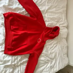 En röd oversized hoodie med en mysig och stor luva, en text där det står ”the beginning is the end” i en cirkel. Den är lite sönder i muddarna i ärmarna 