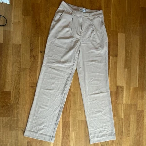 Beiga kostymbyxor med vita ränder från NA-KD - Ett par fina beiga kostymbyxor med vita ränder från NA-KD. I fint skick! Storlek 36
