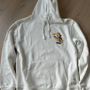 Vit hoodie, oanvänd - Antingen gillar man den eller inte! Vit hoodie med orange tryck. Aldrig använd. Storlek XS.