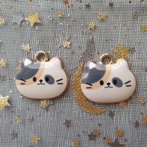 2st flerfärgad katt berlock, hängsmycke  - Berlocker, hängsmycke  Motiv: flerfärgad katt  Färg: vit, grå, orange och guldfärgade baksida  Antal: 2st  Skick: nya/oanvända  Går tex att sätta dem på halsband, armband eller göra örhängen av dem.  Eller använda till annat pyssel 