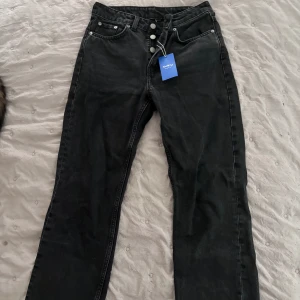 Svarta jeans  - Mörka jeans från weekday i storlek 26/30. Midjemått : 74 cm. Köpt från Sellpy men sellpy prislapp kvar då de aldrig kommit till användning. Knappgylf, lite urtvättad färg på jeansen 