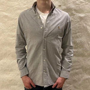 Ralph Lauren skjorta  - Ralph lauren skjorta i färgen grå. Storlek XS och modellen är 178 cm. Nyskick, inga skavanker. Nypris 1299 kr, köp för endast 549kr.