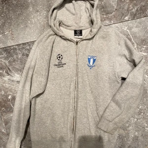 Champions league tröja  - Grå luvtröja i storlek S med dragkedja. Champions league fotboll Malmö FF. Sparsamt använd. Jättefint skick! Rekommenderar!! Säljs pga garderobrensning, kika gärna på mina andra annonser, säljer mycket. Samfraktar gärna:) 