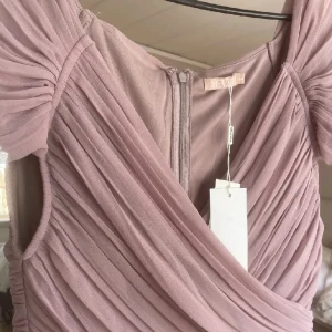 Oanvänd balklänning - Superfin balklänning från Nelly med prislappen kvar! Klänningen är lång, jag är 178 cm och den går ner över fötterna. Färgen är lite ”smutsrosa”, den är kortärmad och går omlott över brösten. Skriv privat för fler bilder 🫶🏻