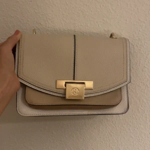 Väska  - Beige & ljusrosa väska med gulddetaljer från River Island. Bandet saknas därav priset 