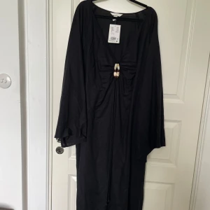Långklänning med pärlutsmyckning - Jättefin svart långklänning från hm med utsvängda ärmar och en pärlutsmyckning man kan knyta runt nacken. Aldrig använd, prislappen kvar<3