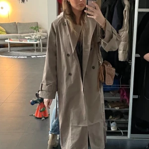 Trenchcoat - Skitsnygg trenchcoat i färgen walnut (beige). Funkar alla säsonger och är i nyskick. Klassisk tidlös stil och fina detaljer. 