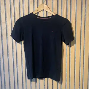 En mörk mörkblå/svart T-shirt från märket Tommy hilfiger. Den är ytterst använd och har inte några defekter. Storleken är xs/156-164 och sitter riktigt stilrena och bekvämt. Kontakta mig vid frågor 