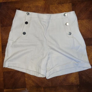 Shorts med knappar - Shorts i färgen beige. Knappar på sidorna. 