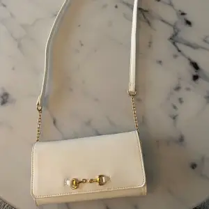 Jag säljer denna jättefina vita handväskan med guldiga detaljer💕 Aldrig använt, men den har fått några fläckar på baksidan men syns inte när den används. Köpt på glitter för 250 kr för något år sedan💗