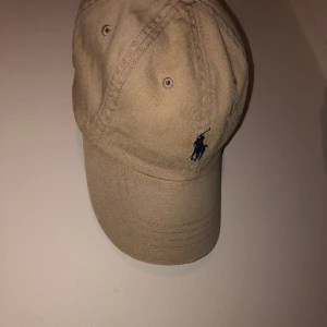 Ralph lauren keps - Beige Ralph lauren keps som säljs då den inte längre används. Inte använts så säljes därför. Ren och fräsch ändast litet märke i fram, men ingenting som syns så mycket. Skriv för mer bilder!
