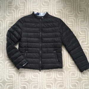 Vändbar Svart lättviktj dunacka Armani. Nyskick. FYND! - Underbar lätt och mjuk, vändbar dunjacka - perfekt för vår, höst och lite kyliga sommardagar!  Original Emporio Armani. Mycket hög kvalitet. Italiensk Strl. 48, ca 40.  Längd: 60 cm, br. 50 cm Tvä invändiga fickor. Blixtlåset är delbart åt båda håll