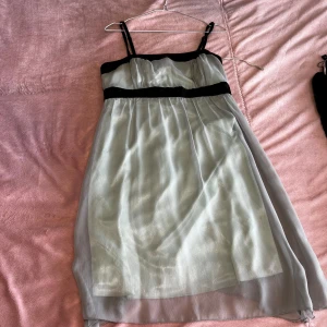 Klänning  - Verkar vara i färgen turkos och vit. Den har svarta pärlor vid bröstet som man kan se på bilden. Den finns i storlek 38. Finns i värsta Stockholm 