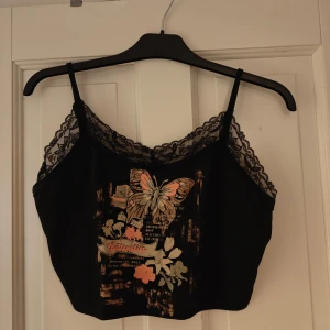 Svart kort linne med tryck  - Linne med tryck och spetsdetaljer Slutar typ strax vid/ovanför naveln  Använd fåtal gånger Justerbara axelband