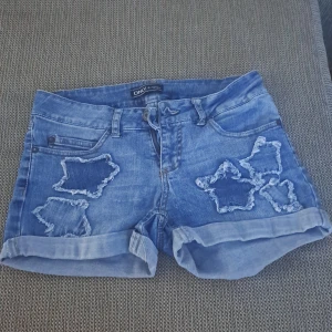 Blå jeansshorts från ONLY - Blå jeansshorts från ONLY med slitna detaljer och uppvikta ben. Shortsen har fem fickor och en knapp- och dragkedjestängning framtill.