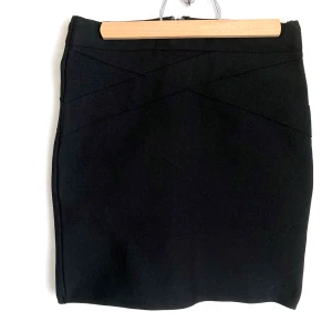 Svart minikjol, stl. XS 34, bodycon - Svart minikjol från Bik Bok i stabilt stretchmaterial, dragkedja bak. Dekorbandet har släppt en aning bak samt noppor fram. Mått i cm: midjevidd 31; höftvidd 37; längd 40.