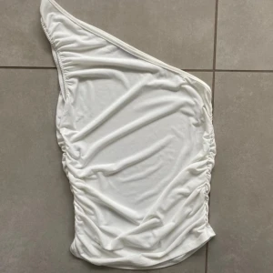 One shoulder top - Så snygg vit one shoulder topp. Tight, men väldigt stretchig så anpassar sig bra efter olika kroppar. Perfekt för massa olika tillfällen, både att klä upp till fest eller klä ner till vardags. 