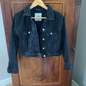 Svart jeansjacka - Svart blekt croppad jeansjacka från PULL&BEAR. Fickor o knappar framtill. Storlek medium men sitter mer som Xs/S