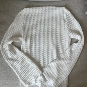 Långärmad topp  - Topp med strukturerat material. Långärmad. Rakt skuren vid halsen, utsvängda och långa armar. Aldrig använd. 