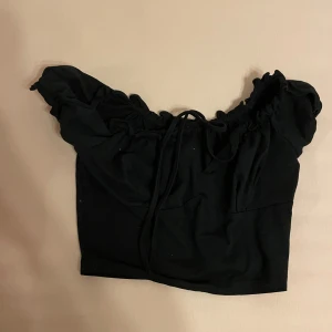 Svart kortärmad topp från Shein - En svart kortärmad topp från Shein med rynkade detaljer och knytning framtill. Toppen har en elastisk halsringning och är croppad. Skriv gärna om ni har frågor 💕