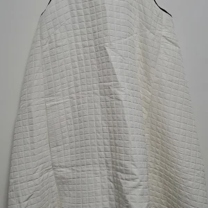 Vit klänning med rutmönster - En vit klänning med ett rutmönster och svarta detaljer vid axlarna. Klänningen har en lös passform och är ärmlös.