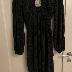 Svart klänning - En elegant svart klänning med långärmad design. Klänningen har en v-ringad hals och är tillverkad i ett veckat material som ger en fin struktur. Passar perfekt för festliga tillfällen. superfin köpt för 300kr o den är inte andvänd ändats provad! pris kan diskuteras bara höra av er!💓