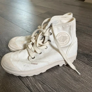 Vita kängor från Palladium - Ett par vita kängor från Palladium med snörning. Skorna har en rund tå och en robust sula. De är tillverkade i ett slitstarkt material och har en logotyp på sidan. Behövs en tvätt, kan göras innan de skickas vid önskan