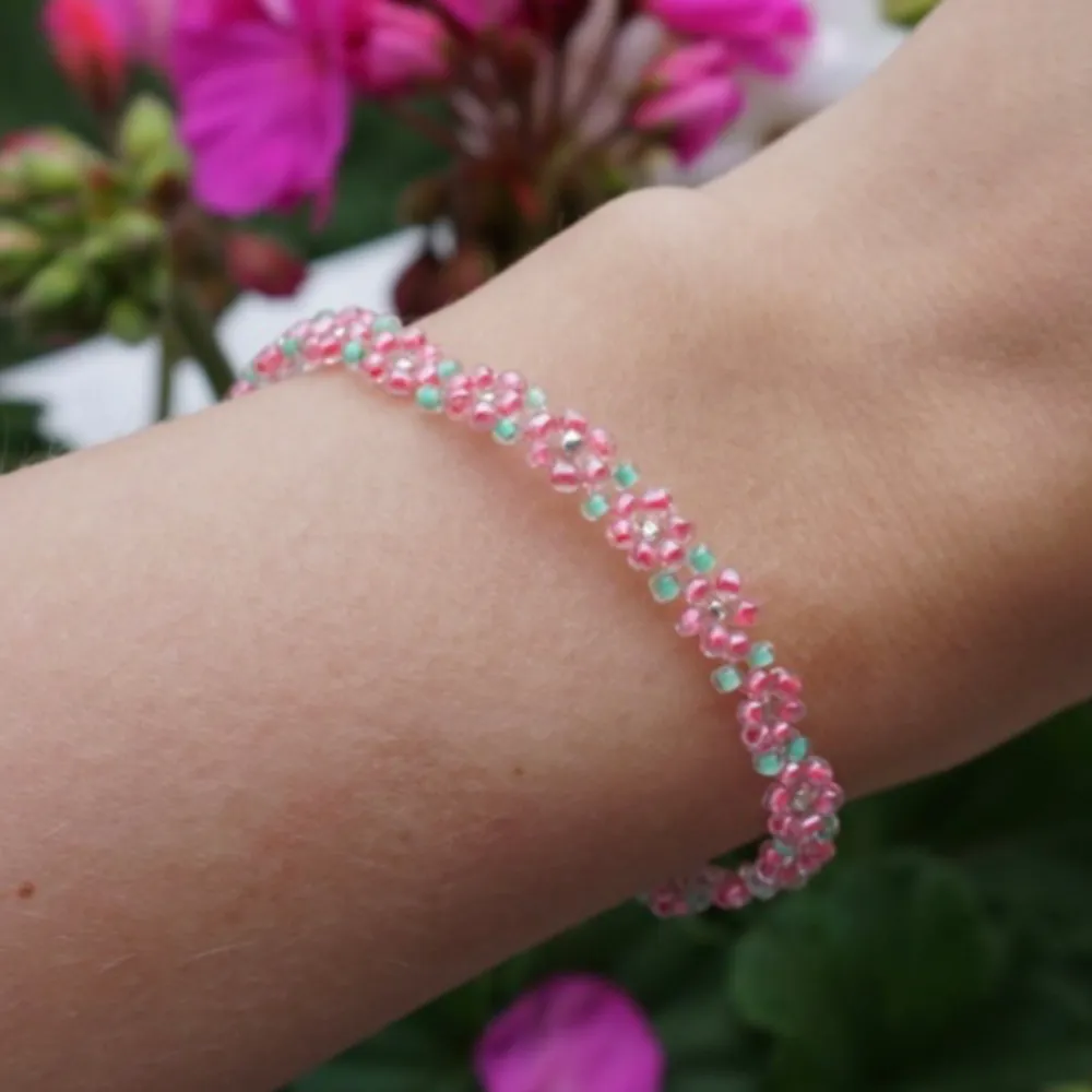 Armband som är pärlat förhand med rosa blommor och gröna blad som detaljer. Finns även silverfärgade detaljer. Armbandet har en knäppning i silver. . Accessoarer.