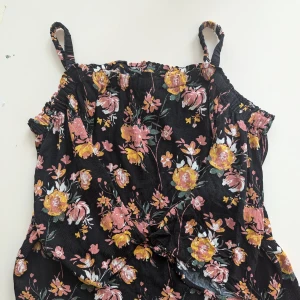 Blommig linnetopp från My Wear - En svart linnetopp från My Wear med ett blommigt mönster i rosa och gula nyanser. Toppen har smala axelband och är tillverkad av 100% viskos.