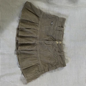 Grå Manchester Kjol - Veckad Manchesterkjol från Minga London i fint skick. 100% bomull. Det står S men den passar mig som ofta har M. Midja: 37 cm Längd: 33 cm