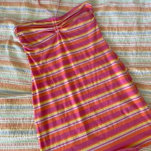 Randig sommarklänning - En färgglad randig sommarklänning med smala axelband. Klänningen har ränder i rosa, orange, gul och vit. Den är ärmlös och har en åtsittande passform.
