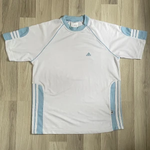 Y2K Adidas Tränings T-shirt - Har en subtil fläck vid magen på framsidan, se sista bilden. Annars fint skick.  Mått: Byst (pit to pit): 52cm Fåll: 52cm Ärmar 36cm Längd (nacksömmen ner): 52cm Skriv om fler bilder önskas.