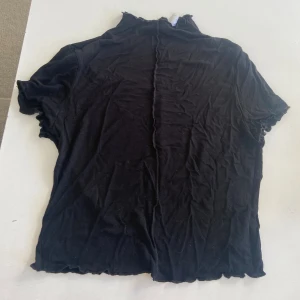 DIVIDED tshirt svart (M) - Svart T-shirt från H&M med hög krage, vågiga kanter och stygn i mitten, storlek M. Tröjan är använd endast ett fåtal gånger och passar perfekt till fest och vardag 🖤