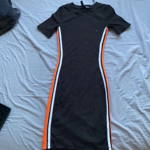 Svart klänning  - Fin svart klänning med vita och oranga sträck på sidorna💗 Köpt 2020 för en halloween fest men har inte riktigt använt sen dess. Tror original pris är 200 men är inte helt säker 🤍pris går att diskuteras 